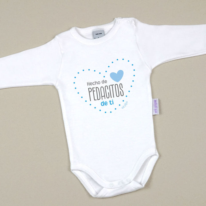 Body blanco de algodón para bebé con manga larga y texto azul "Hecho de pedacitos de ti" decorado con un corazón y puntos.