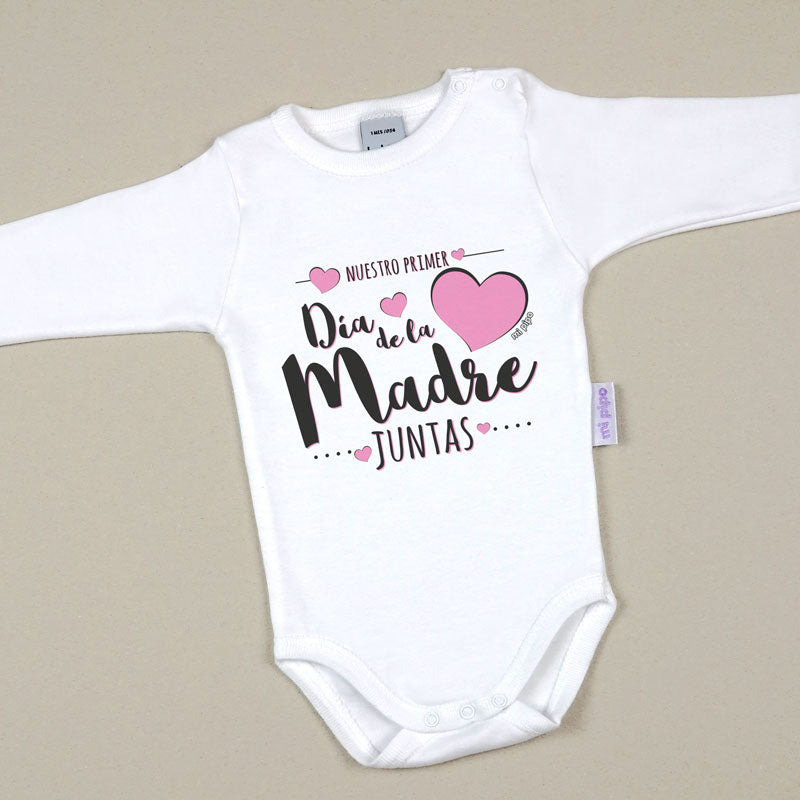 Body blanco para bebé con manga larga, texto rosa y negro "Nuestro primer Día de la Madre juntas" y corazón rosa.