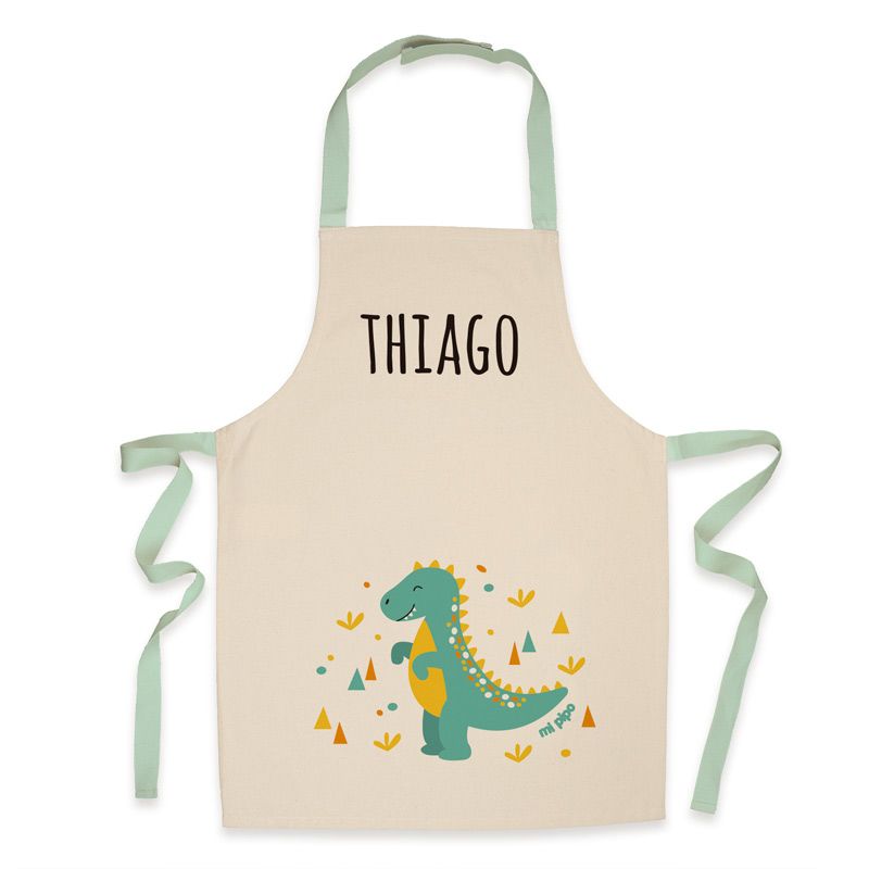 Delantal infantil crema de algodón con tirantes verdes, estampado de dinosaurio verde y nombre personalizado "Thiago" en.