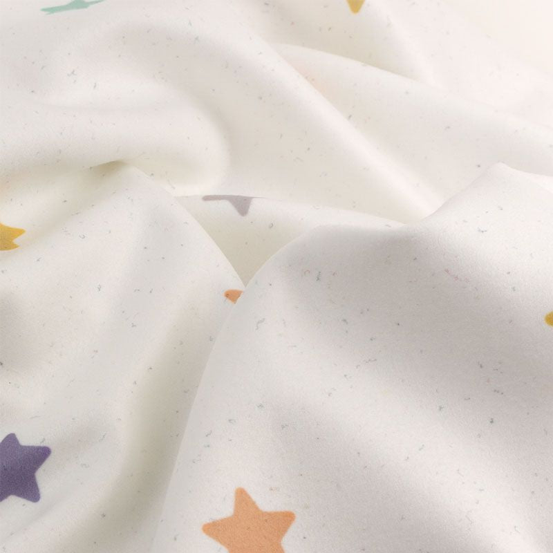 Manta suave blanca con estampado de pequeñas estrellas en tonos pastel como lila, mostaza y verde.
