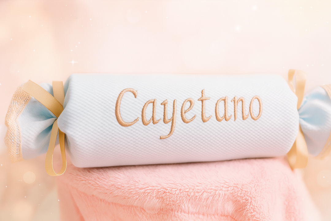 Cojín antivuelco blanco con bordado beige "Cayetano" y detalles de encaje y lazo beige en los extremos.